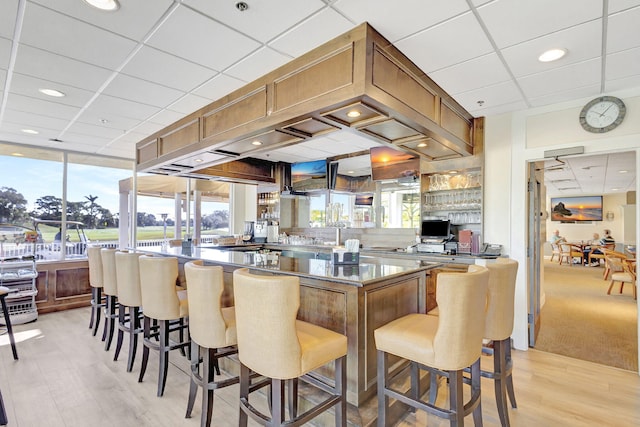 kitchen with a paneled ceiling, a breakfast bar, and light wood-type flooring