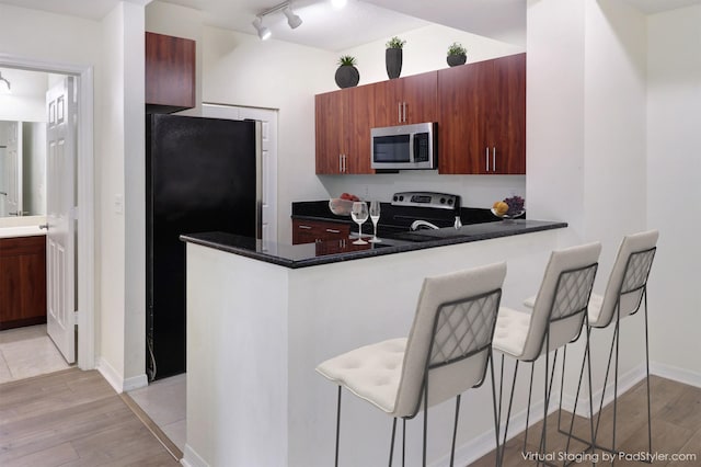 kitchen featuring dark countertops, stainless steel appliances, a breakfast bar, and light wood-type flooring