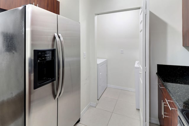 kitchen featuring stainless steel refrigerator with ice dispenser, washer and clothes dryer, light tile patterned floors, dark stone countertops, and modern cabinets