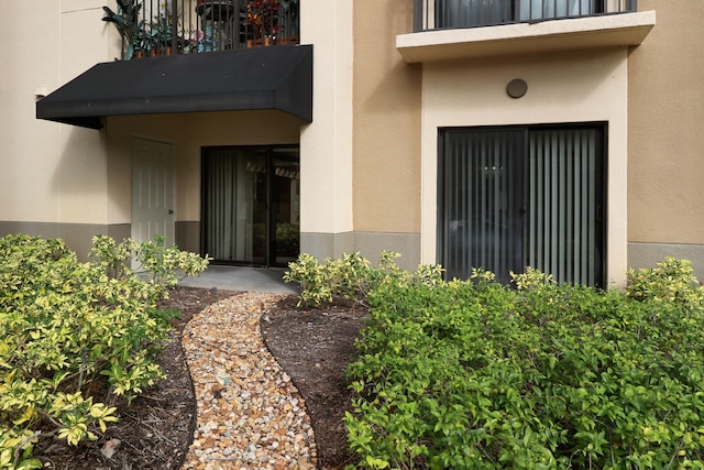 view of exterior entry with a balcony and stucco siding