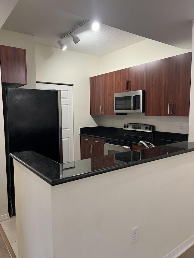 kitchen with kitchen peninsula, rail lighting, appliances with stainless steel finishes, and dark stone counters