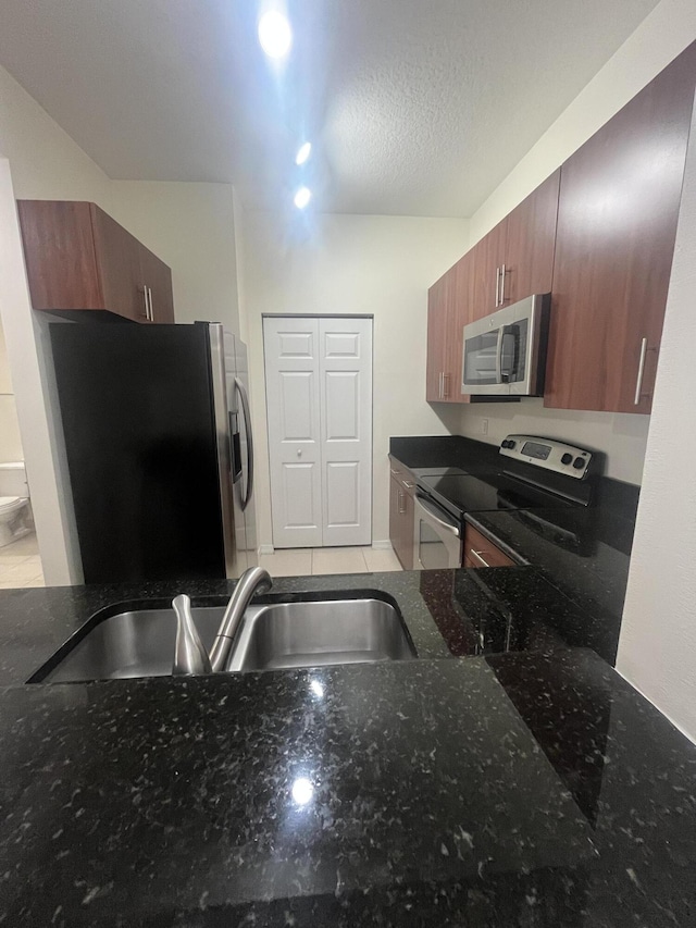 kitchen featuring a textured ceiling, stainless steel appliances, dark stone counters, and sink