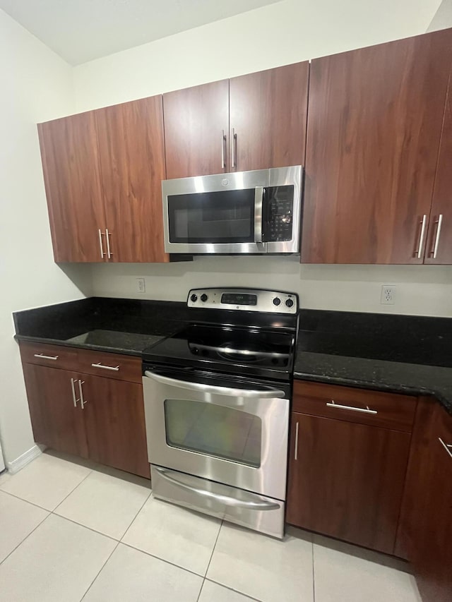 kitchen with appliances with stainless steel finishes, light tile patterned floors, and dark stone counters