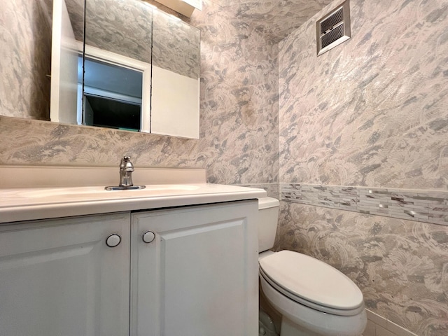 76 Sheffield D, West Palm Beach, FL 33417 - half bathroom featuring wallpapered walls, vanity, toilet, and wainscoting