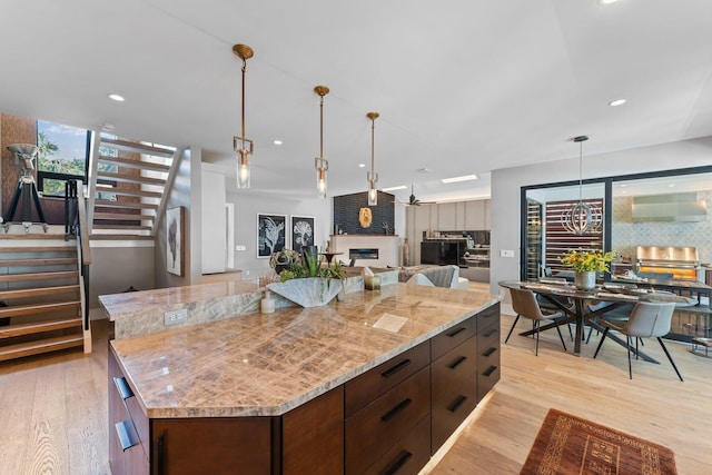 kitchen featuring a large island, a large fireplace, light stone counters, and light hardwood / wood-style flooring