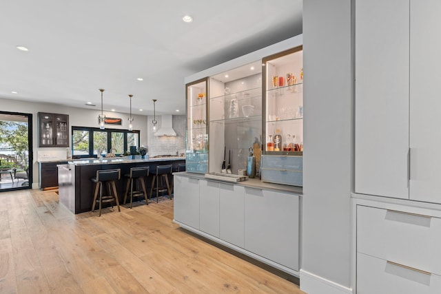 bar featuring decorative backsplash, light hardwood / wood-style floors, hanging light fixtures, and wall chimney range hood