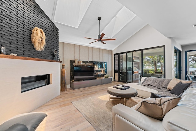 living room with light wood-type flooring, a skylight, a large fireplace, ceiling fan, and wooden walls