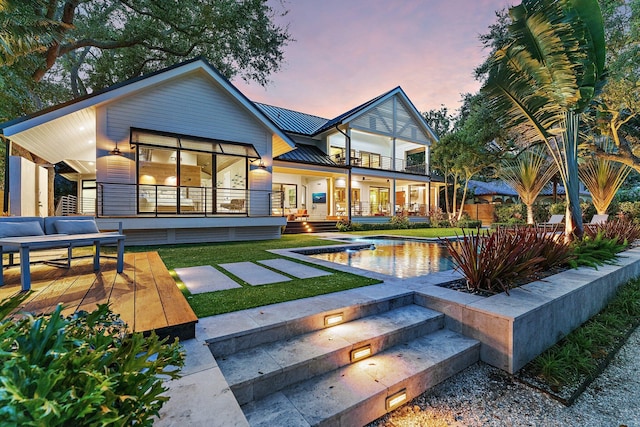 back house at dusk featuring a yard, an outdoor living space, a balcony, and a patio