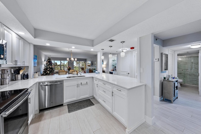 kitchen featuring kitchen peninsula, light wood-type flooring, appliances with stainless steel finishes, decorative light fixtures, and white cabinetry