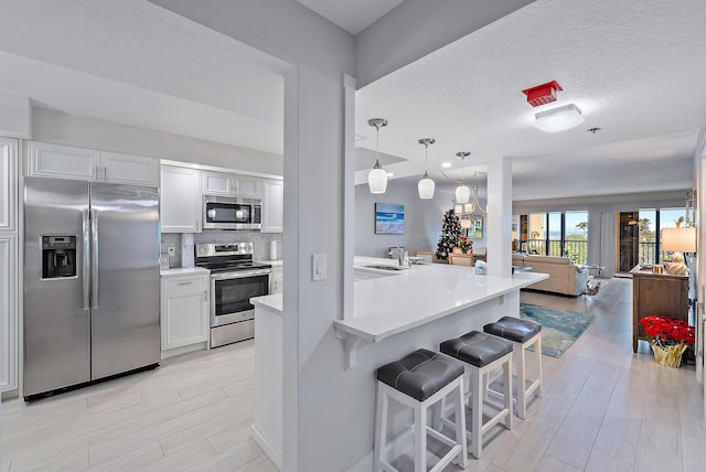 kitchen with white cabinets, appliances with stainless steel finishes, a kitchen bar, and decorative light fixtures