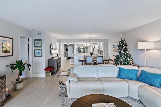 living room with a textured ceiling, an inviting chandelier, and light hardwood / wood-style flooring