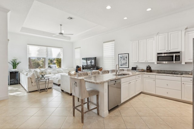 kitchen featuring a kitchen bar, sink, appliances with stainless steel finishes, light stone counters, and white cabinetry