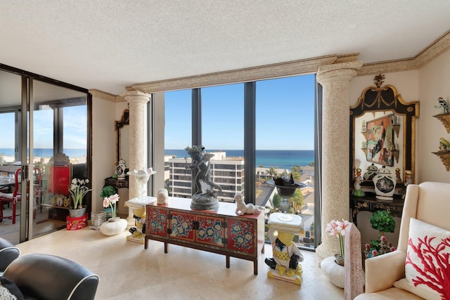 living room featuring a textured ceiling, a water view, ornate columns, and a wall of windows