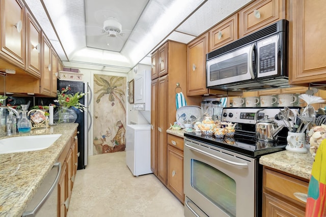 kitchen with light stone countertops, appliances with stainless steel finishes, ceiling fan, sink, and washer / dryer