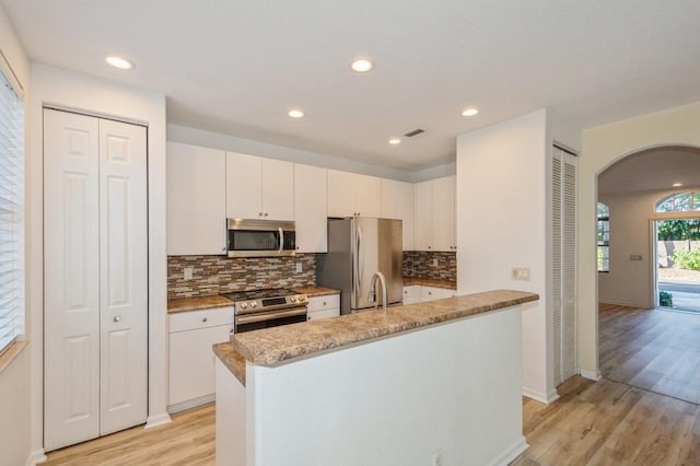 kitchen featuring light wood-type flooring, stainless steel appliances, white cabinetry, and an island with sink