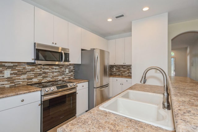 kitchen featuring white cabinets, appliances with stainless steel finishes, decorative backsplash, and sink