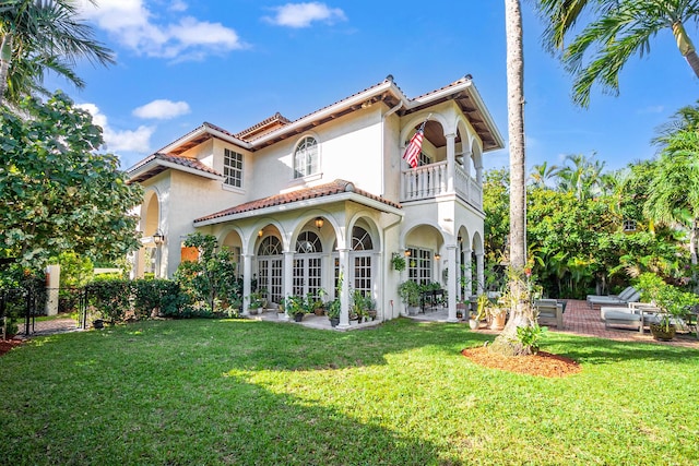 rear view of property with a lawn, a patio area, and a balcony