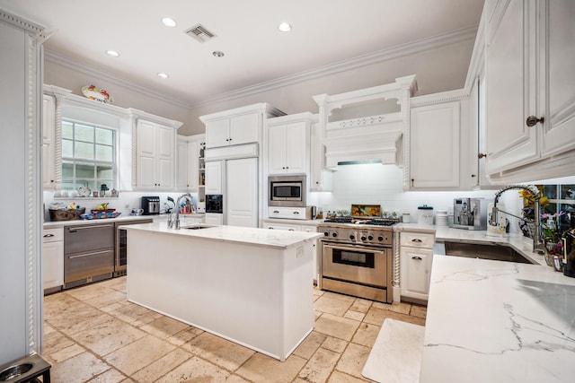 kitchen with built in appliances, a center island with sink, white cabinetry, and sink