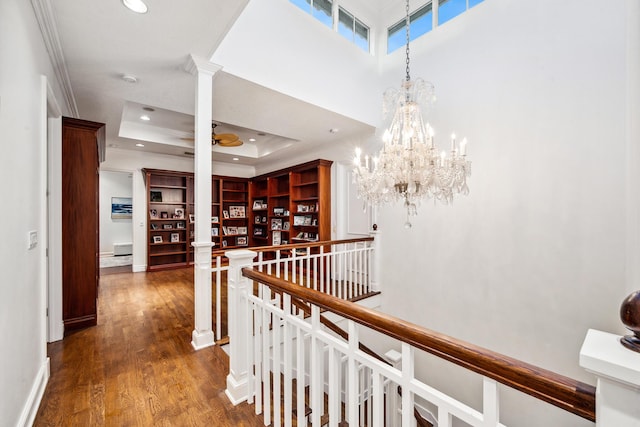 corridor featuring decorative columns, a raised ceiling, crown molding, a notable chandelier, and dark hardwood / wood-style floors