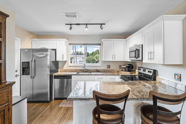 kitchen with kitchen peninsula, sink, white cabinets, and appliances with stainless steel finishes