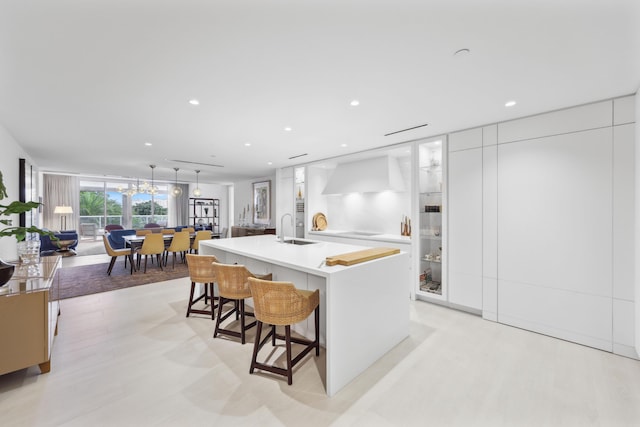 kitchen featuring a kitchen breakfast bar, wall chimney exhaust hood, sink, white cabinets, and an island with sink