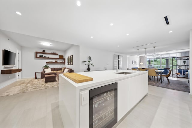 kitchen featuring white cabinets, a center island with sink, sink, and wine cooler