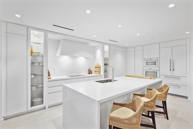 kitchen featuring a kitchen breakfast bar, sink, an island with sink, double oven, and white cabinetry