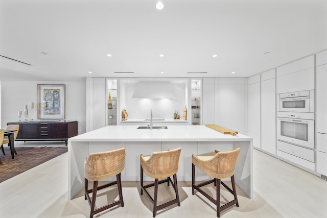 kitchen with a breakfast bar, white double oven, sink, a large island, and white cabinetry