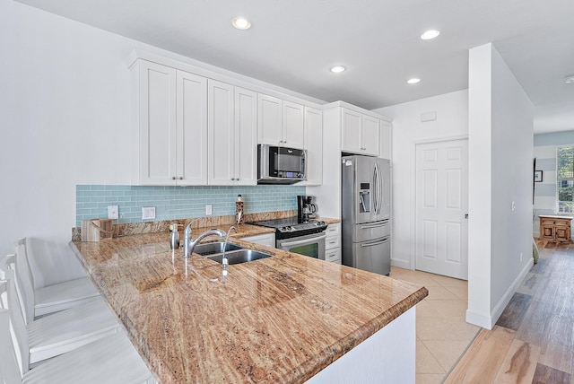 kitchen with kitchen peninsula, stainless steel appliances, sink, white cabinets, and light hardwood / wood-style floors