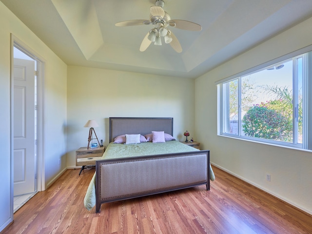 bedroom with wood-type flooring, a raised ceiling, and ceiling fan