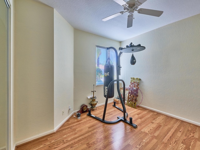 workout room with a textured ceiling, light wood-type flooring, and ceiling fan