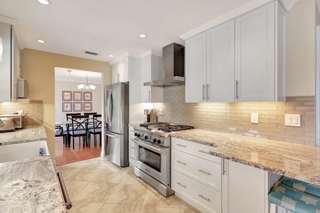 kitchen featuring visible vents, stainless steel appliances, white cabinetry, wall chimney exhaust hood, and a notable chandelier