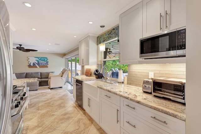 kitchen with open floor plan, decorative backsplash, appliances with stainless steel finishes, white cabinetry, and a sink