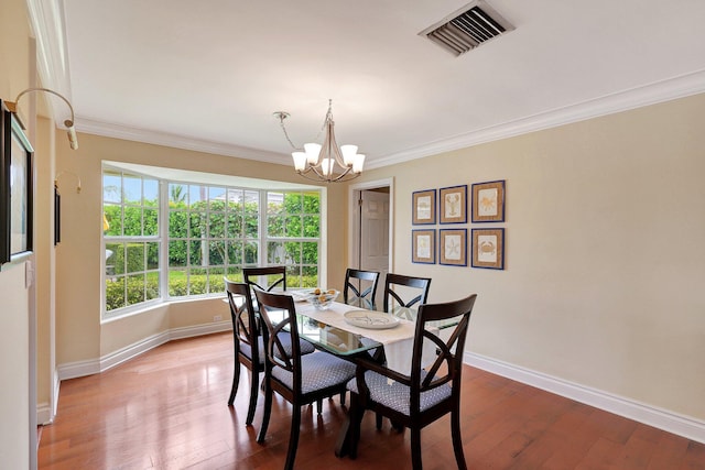 dining space featuring visible vents, wood-type flooring, an inviting chandelier, and ornamental molding