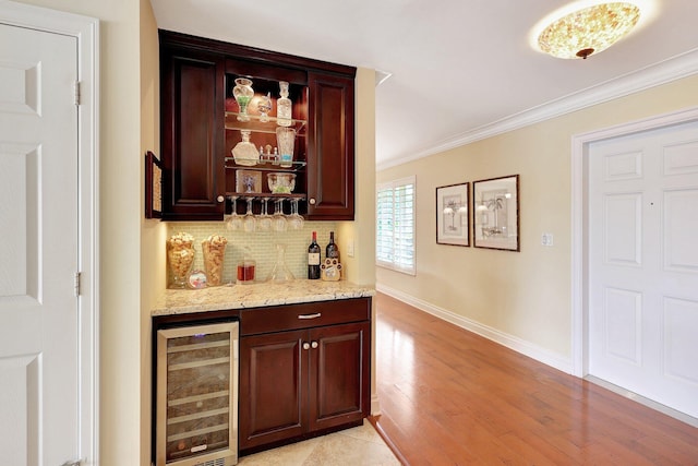 bar with beverage cooler, light wood finished floors, a bar, decorative backsplash, and crown molding