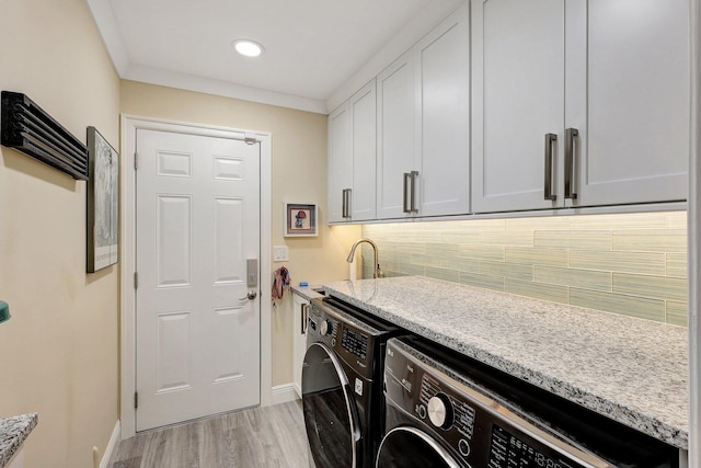 clothes washing area featuring washer and dryer, baseboards, cabinet space, and light wood-style floors