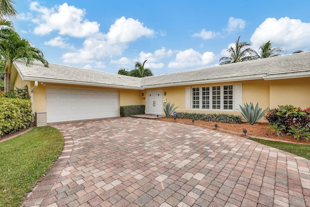 ranch-style house featuring stucco siding, an attached garage, and decorative driveway