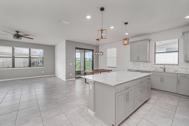 kitchen with gray cabinetry, sink, ceiling fan, decorative backsplash, and a kitchen island