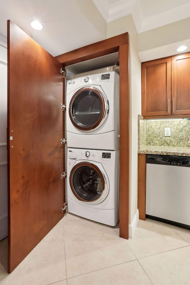 laundry room with stacked washer / drying machine, ornamental molding, and light tile patterned floors