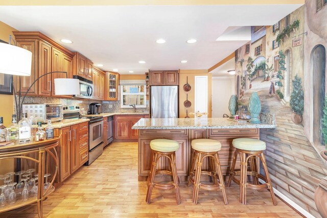 kitchen with light stone countertops, appliances with stainless steel finishes, tasteful backsplash, sink, and light hardwood / wood-style floors