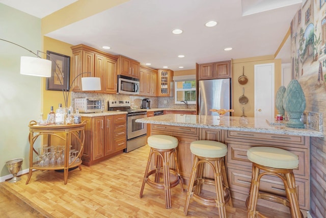 kitchen with a kitchen bar, appliances with stainless steel finishes, kitchen peninsula, sink, and light hardwood / wood-style flooring