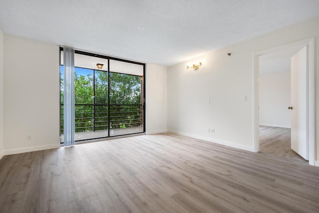 spare room with a wall of windows, light wood-type flooring, and a textured ceiling