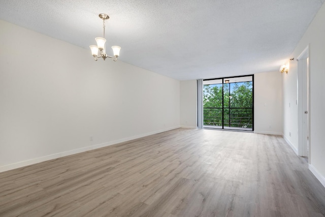 unfurnished room featuring expansive windows, an inviting chandelier, a textured ceiling, and light wood-type flooring