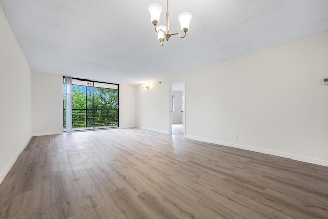 empty room with hardwood / wood-style floors, expansive windows, a textured ceiling, and an inviting chandelier