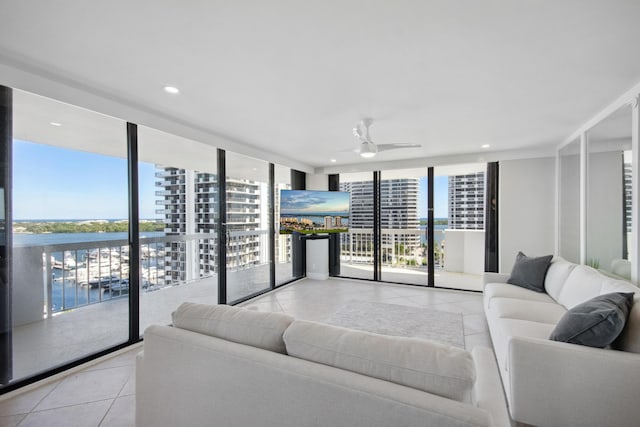 tiled living room featuring expansive windows, ceiling fan, and a water view