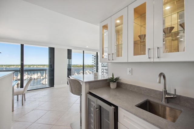 kitchen featuring beverage cooler, sink, a water view, white cabinetry, and light tile patterned flooring