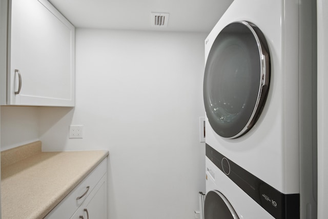 clothes washing area featuring cabinets and stacked washing maching and dryer