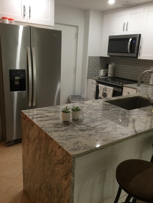 kitchen with white cabinetry, light stone countertops, sink, stainless steel appliances, and light tile patterned flooring