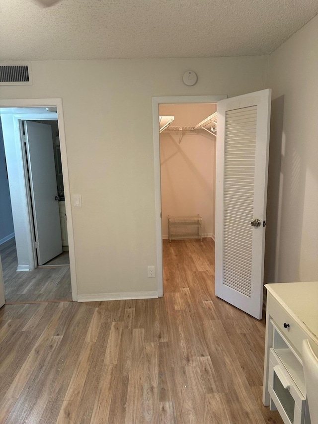 unfurnished bedroom featuring a spacious closet, a closet, a textured ceiling, and light wood-type flooring