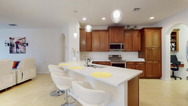 kitchen featuring kitchen peninsula, a kitchen bar, stainless steel appliances, sink, and pendant lighting